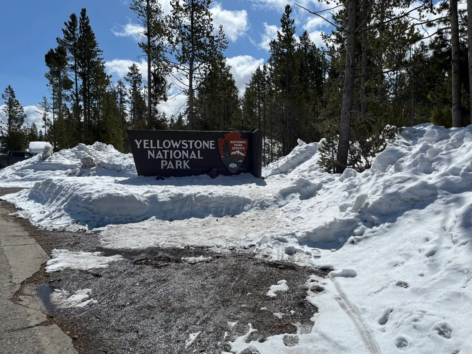 Yellowstone National Park entrance sign covered in spring snow showing seasonal access conditions
