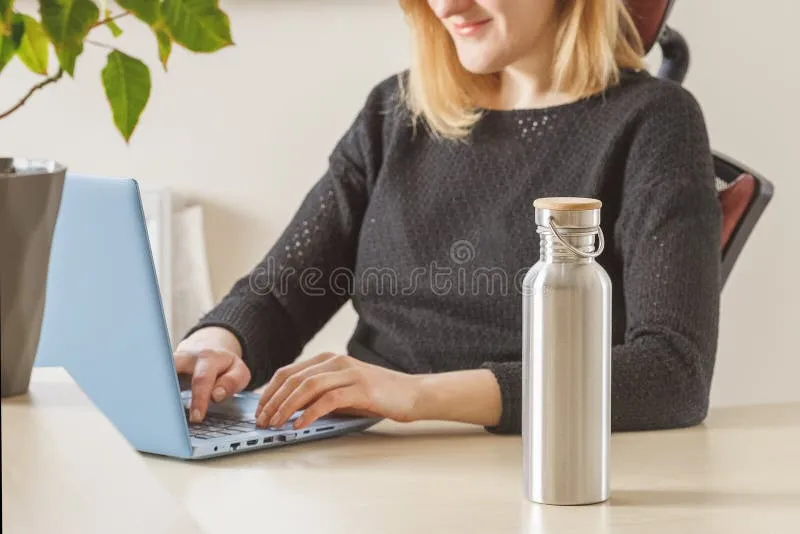 Professional woman using stainless steel water bottle while working from office desk